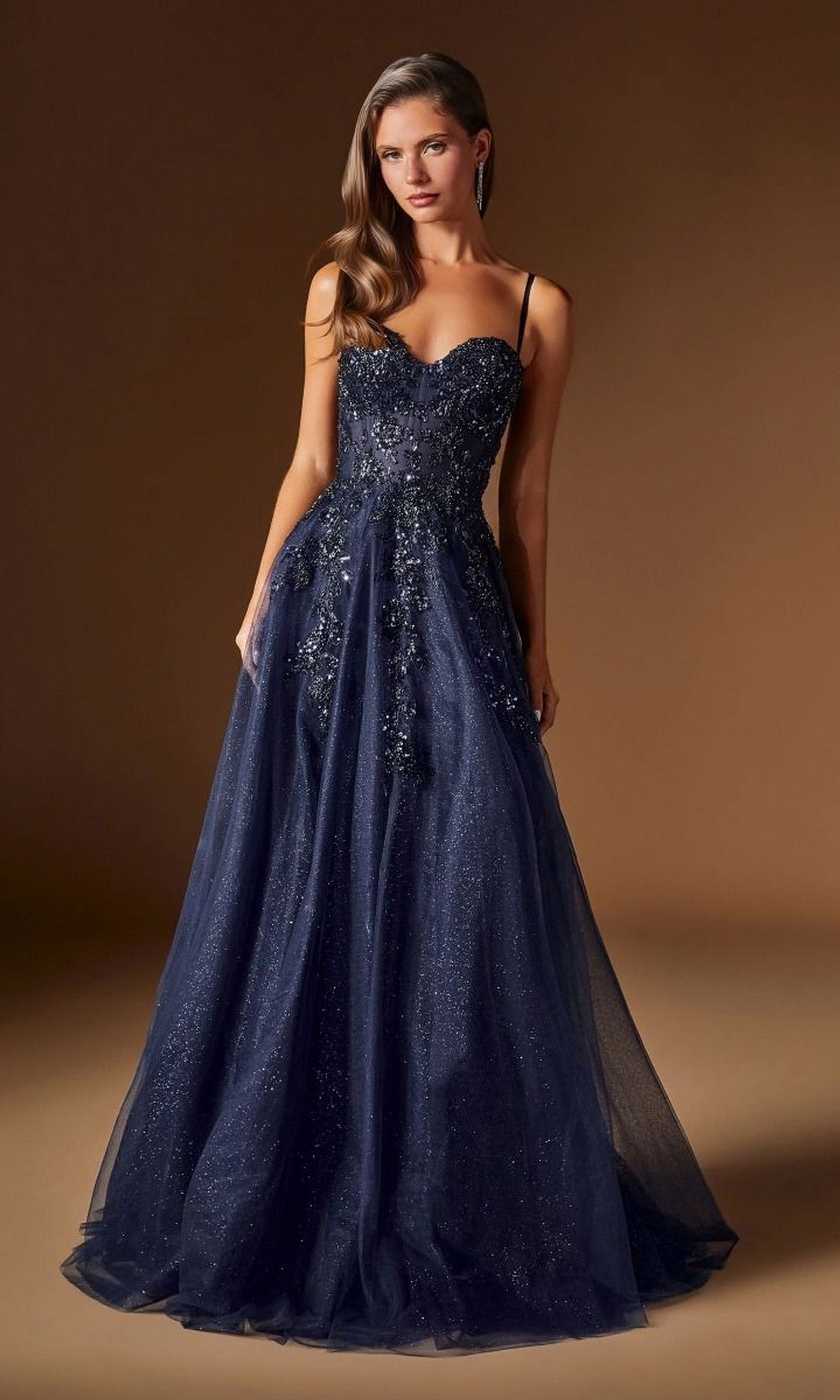 A woman models the Ladivine C177 Long Prom Dress in navy, featuring a fitted embellished bodice and a flowing glitter tulle A-line skirt, standing against a plain brown background.